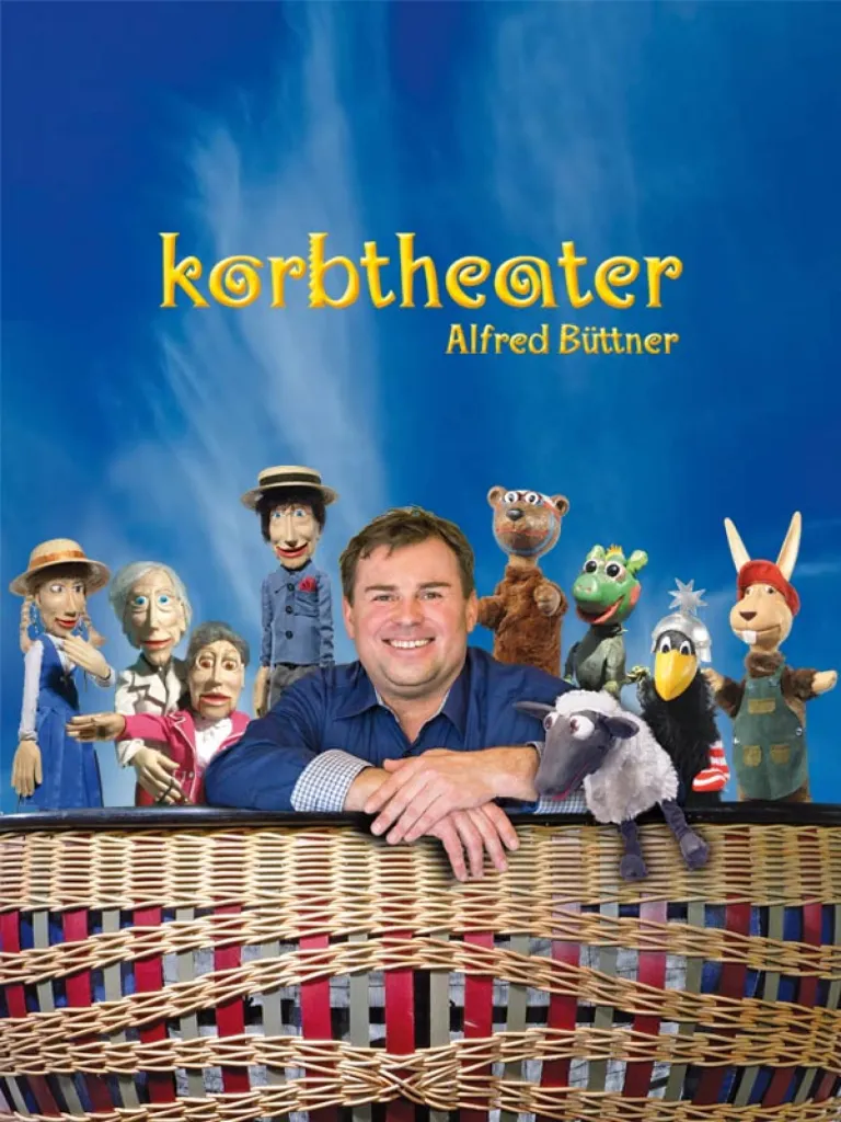 Korbtheater Alfred Büttner: Der Puppenspieler schaut über den Rand seines Weidenkorbs, umgeben von seinen Figuren